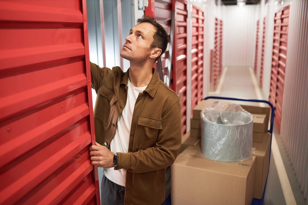 A man inspects storage units in a facility, with red doors and stacked boxes nearby, conveying a sense of organization and curiosity.
