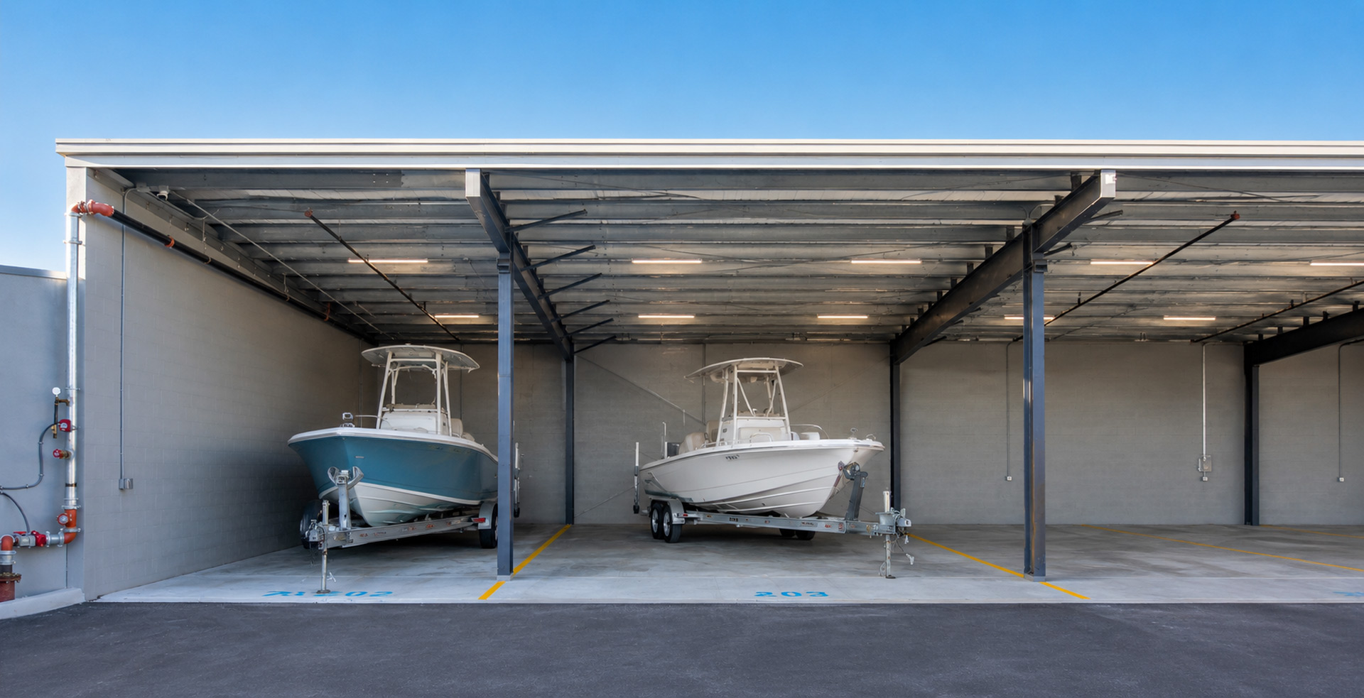 The image shows two boats stored in a modern garage with ample space and overhead lighting, situated under a clear blue sky.