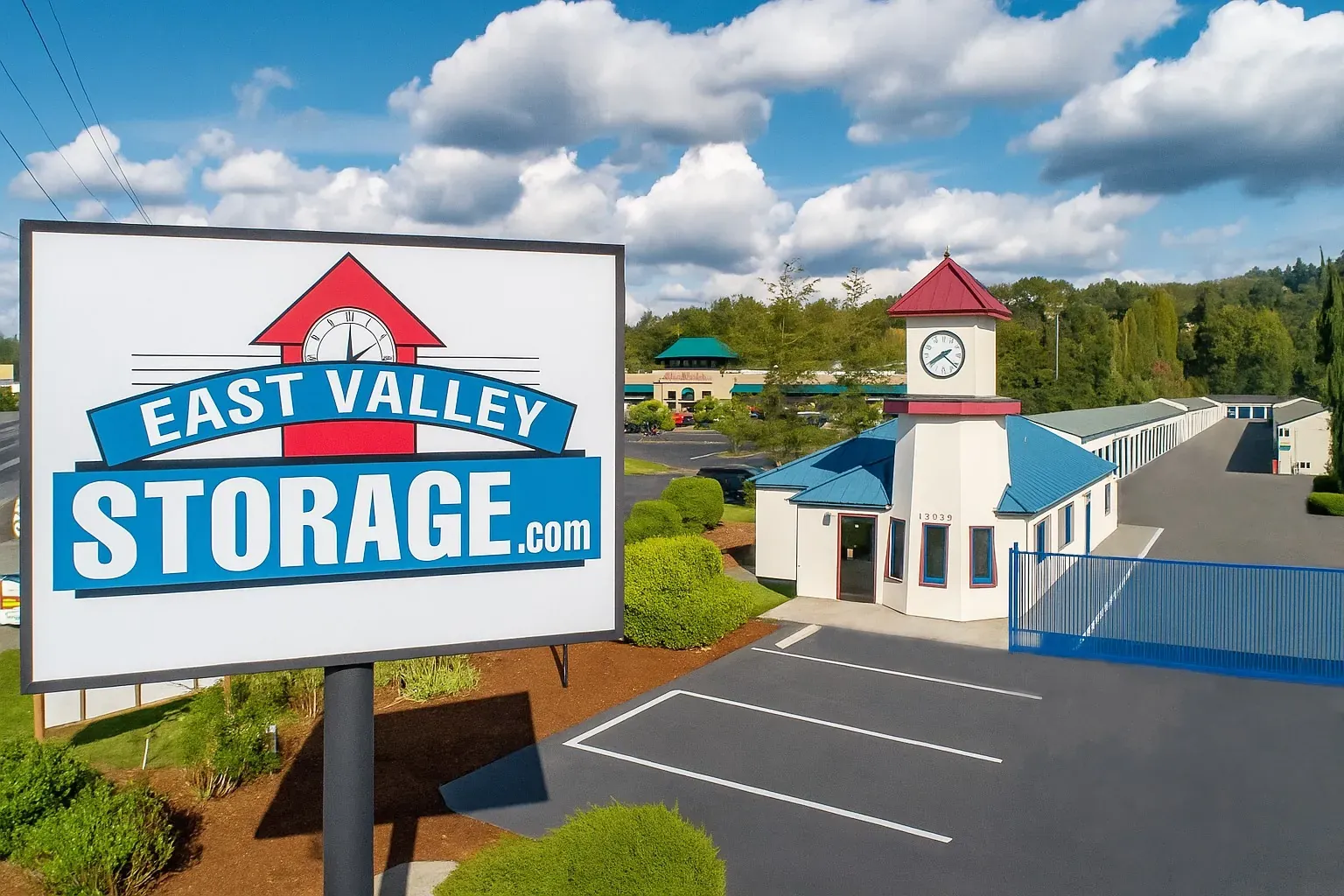 The image shows the East Valley Storage facility, featuring a prominent sign, a clock tower, and well-maintained landscaping under a partly cloudy sky.